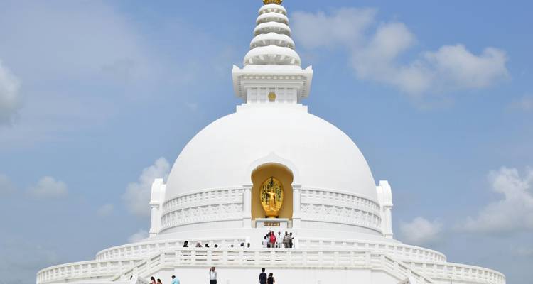 A pristine white stupa with an ornate golden spire against a blue sky.