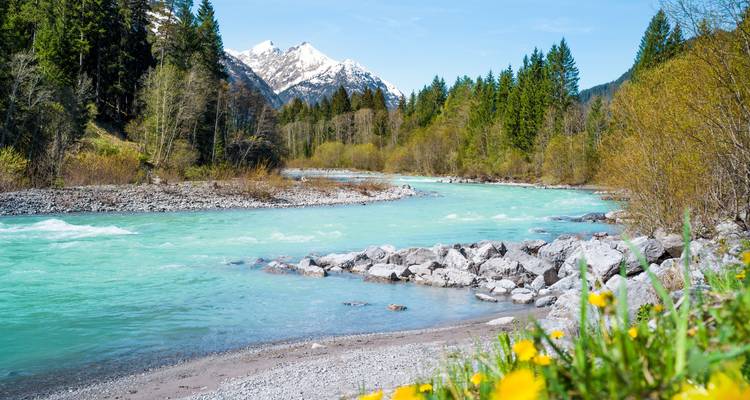 Türkisfarbener Fluss, der durch eine alpine Landschaft mit schneebedeckten Gipfeln fließt.