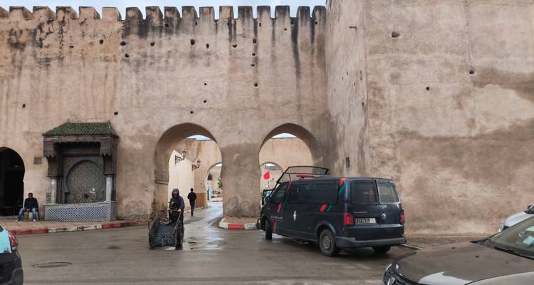Vue extérieure d'une porte de ville fortifiée avec un van qui passe.