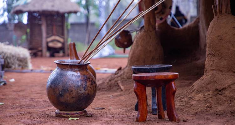 Pot en argile et tabourets au sol dans un cadre culturel.