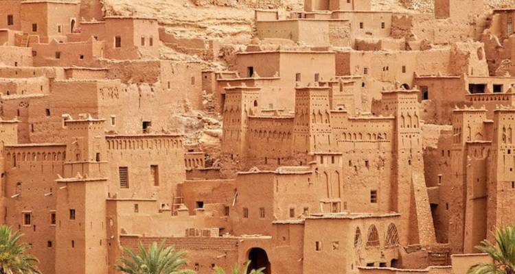 Lehmfarbene historische Gebäude, die in einen Hang hineingebaut sind.