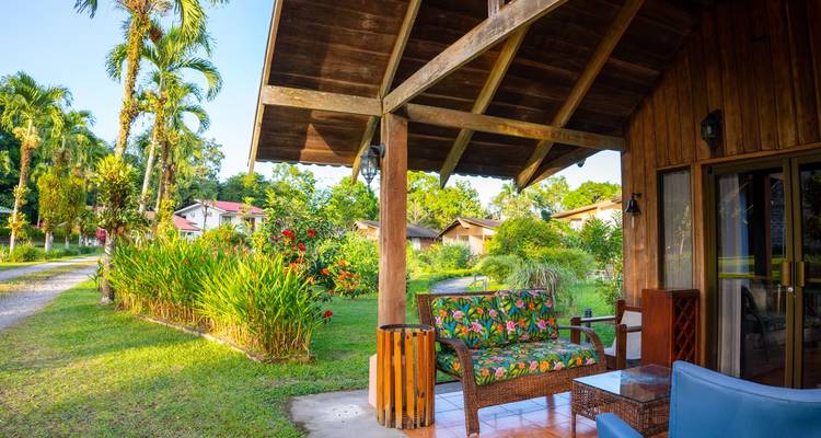 Bungalow rústico de madera con asientos al aire libre coloridos rodeado de jardines tropicales.