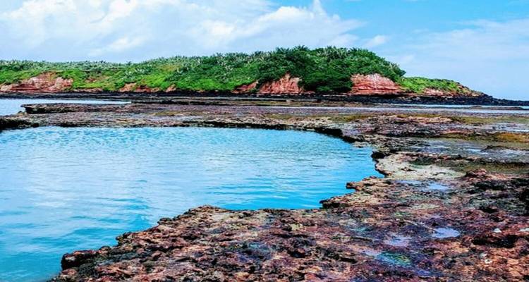 Rotsachtige kustlijn met helder water en kleine begroeiing.