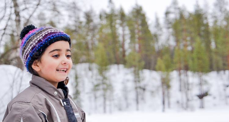 Enfant souriant portant un bonnet tricoté coloré qui profite d'un cadre de forêt enneigée.