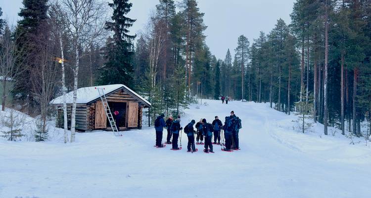 Les raquetteurs se rassemblent près d'un refuge rustique en bois rond le long d'une route forestière enneigée.