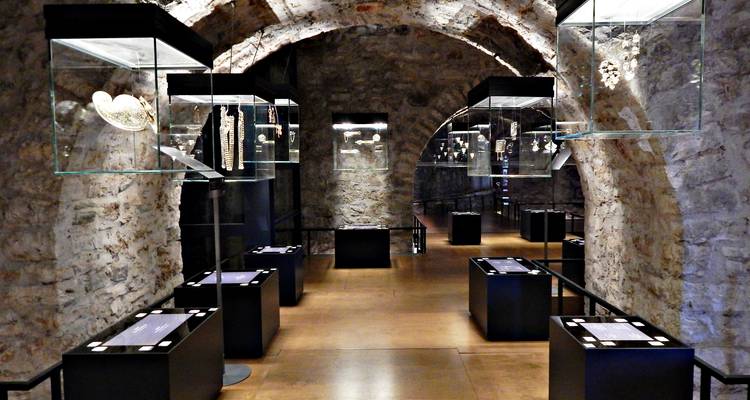 Galería de museo moderno dentro de un pasillo abovedado de piedra que exhibe artefactos en vitrinas de cristal.