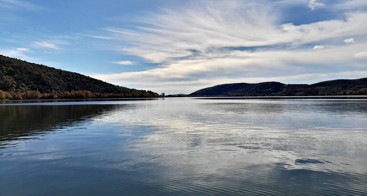 Un lago tranquilo refleja el cielo y las colinas bajas circundantes bajo nubes dispersas.