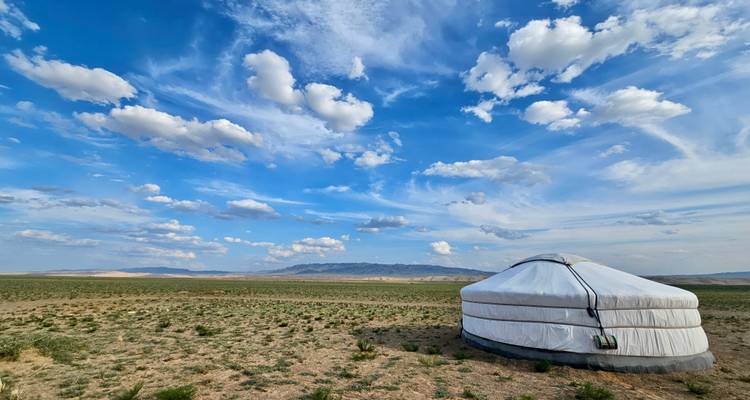Yurta tradicional en un vasto paisaje abierto bajo un cielo azul.