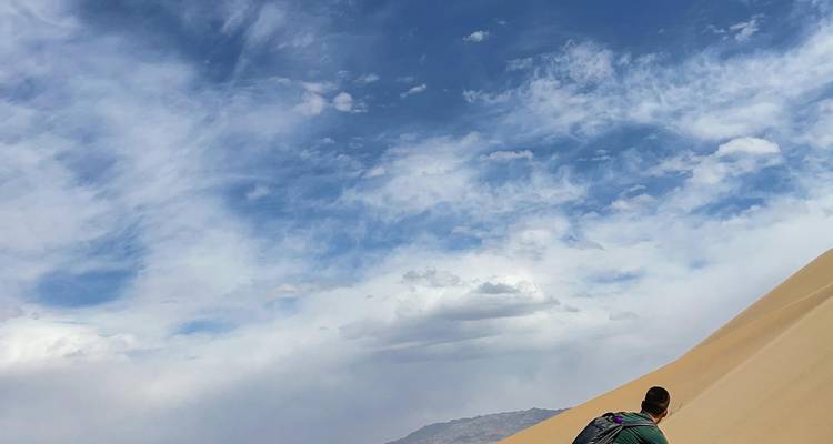 Persona escalando una gran duna de arena con una mochila.