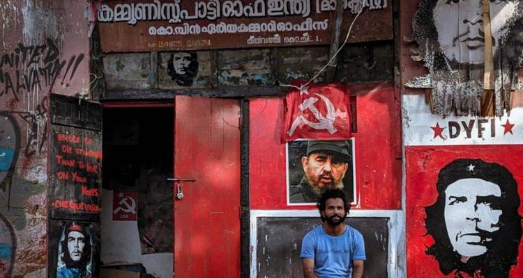 A man sitting in front of a building with murals and communist symbols.