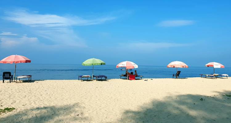 Plage de sable fin avec des parasols colorés et des transats face à une eau bleue et calme.