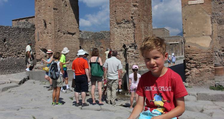 Enfant assis dans des ruines anciennes avec des touristes autour.