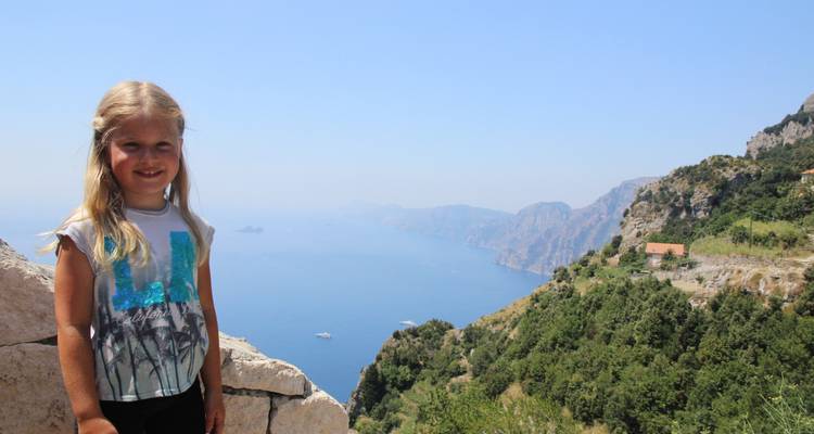Enfant debout sur une corniche surplombant une vue côtière.