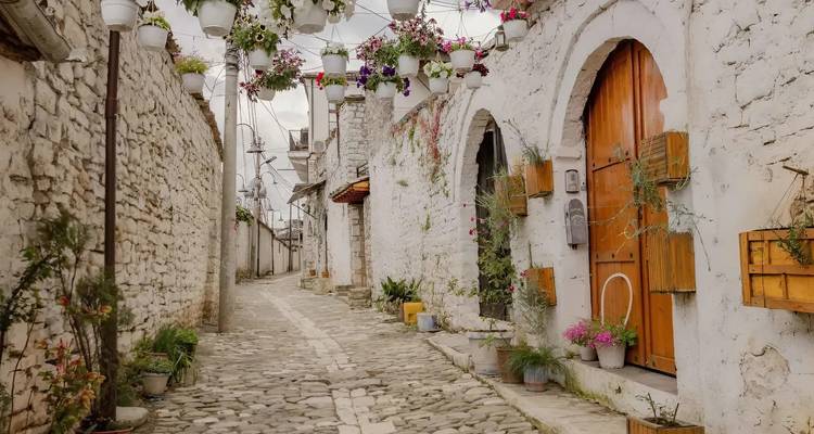 Une rue pavée étroite bordée de bâtiments en pierre blanche décorés de fleurs.