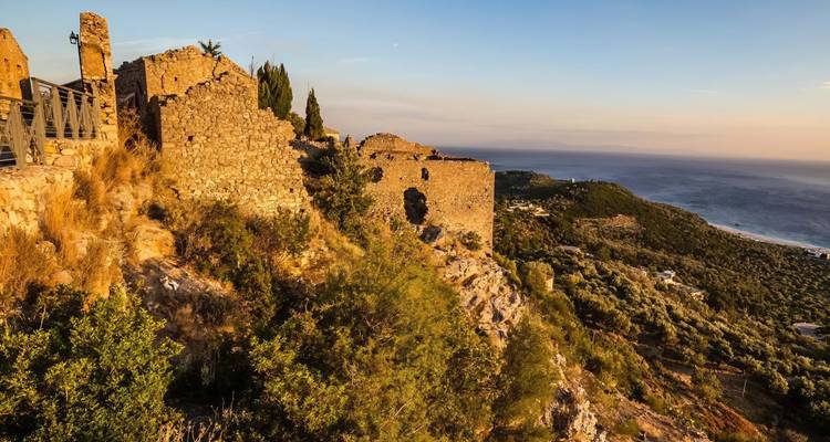 Anciennes ruines de pierre sur une colline surplombant la mer au coucher du soleil.
