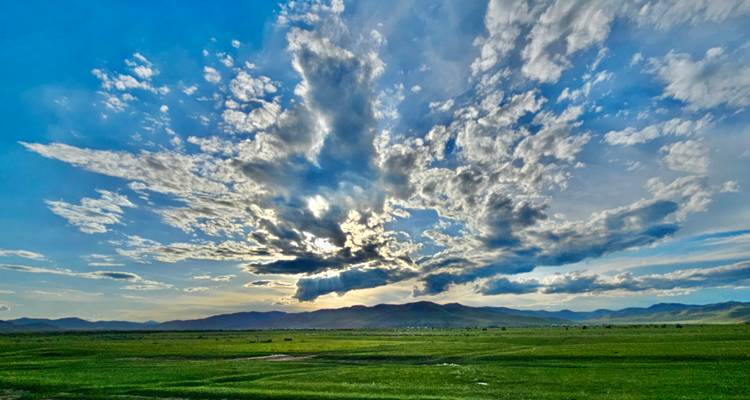 Ciel nuageux au-dessus de plaines vertes avec des montagnes au loin.