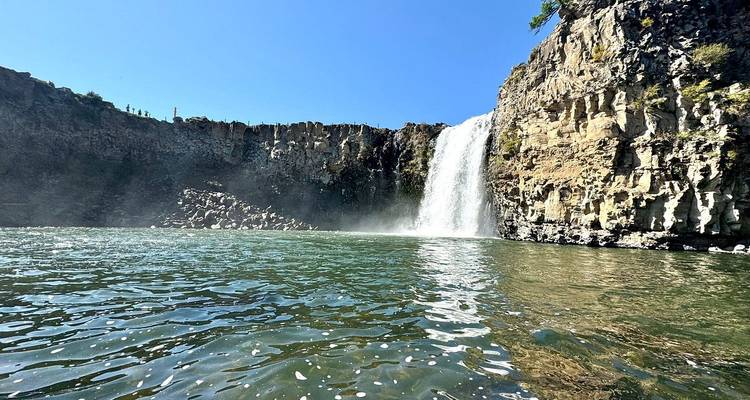 Cascada cayendo en una piscina bajo un cielo azul brillante.