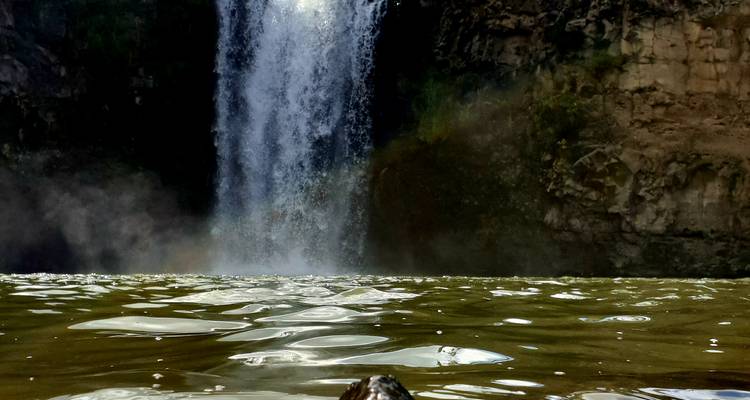 Cascada cayendo en una piscina natural rodeada de acantilados rocosos.