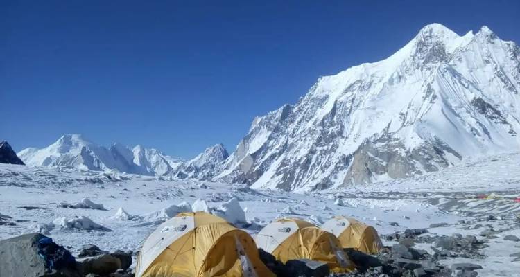Snowy mountains with tents in the foreground under a clear blue sky.