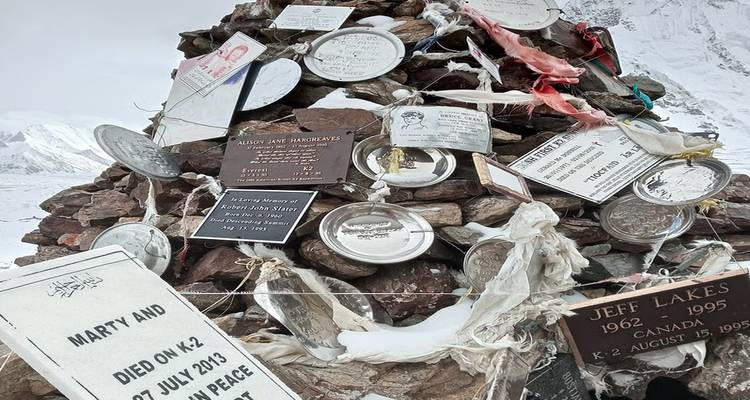 Rock memorial covered with plaques and tokens in a snowy landscape.