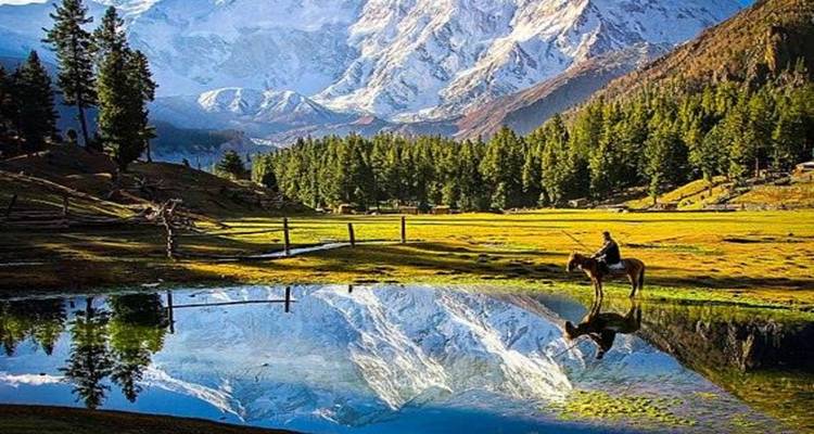 Horse rider near a reflective pond with mountains in the backdrop.