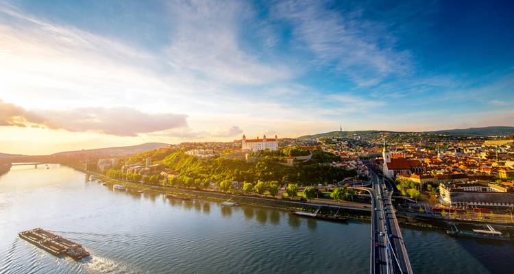 Amplio panorama aéreo del Castillo de Bratislava y el río Danubio bajo una luz de atardecer dramática.