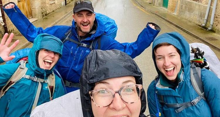 Four people in rain gear excitedly posing for the camera on a wet street.