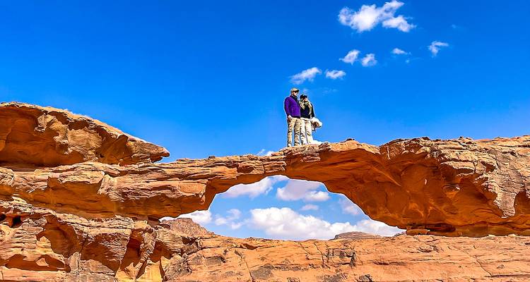 People standing on a natural rock bridge in Wadi Rum.