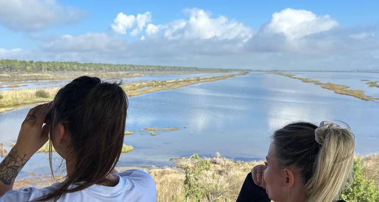 Dos mujeres mirando un vasto lago bajo un cielo nublado.