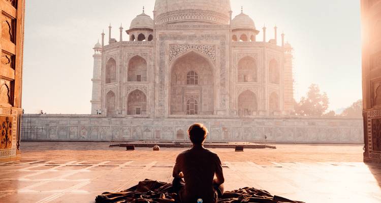 Person sitting and meditating while facing the Taj Mahal from a distance.