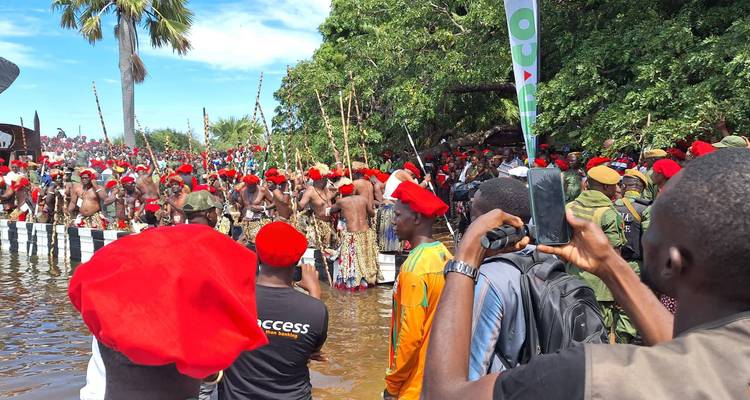 Grande assemblée de personnes en tenue traditionnelle au bord de l'eau.