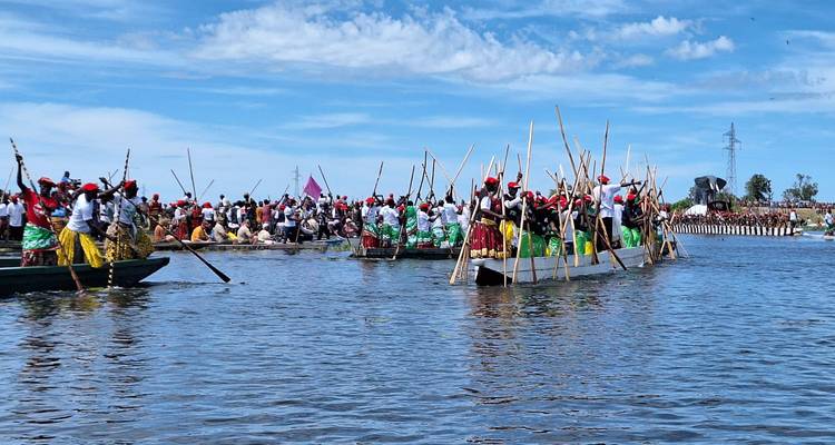 Cérémonie traditionnelle sur des bateaux avec des personnes portant des chapeaux rouges dans un plan d'eau.