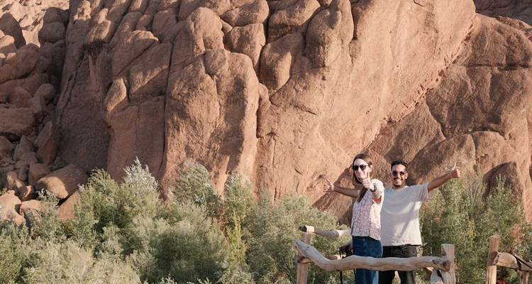 Dos personas posando frente a una gran formación rocosa roja.