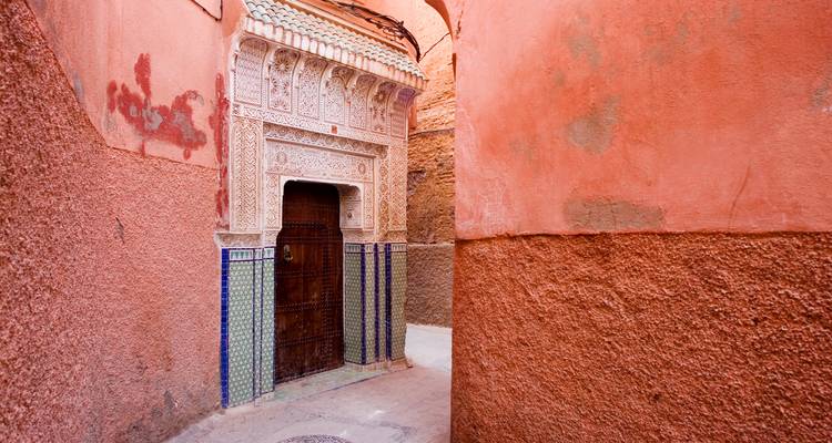 Traditional Moroccan street with ornate door and red-tinted walls.
