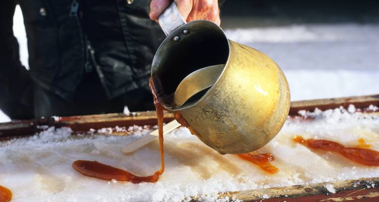 Traditionelle Ahornsirup-Taffy, die auf Schnee gegossen wird, zum Aufrollen auf einem Holzstab.