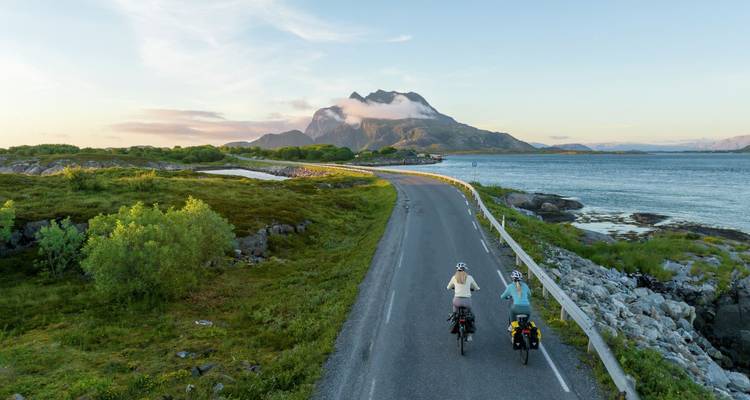 Deux cyclotouristes roulent le long d'une route côtière avec un pic spectaculaire devant eux au coucher du soleil.