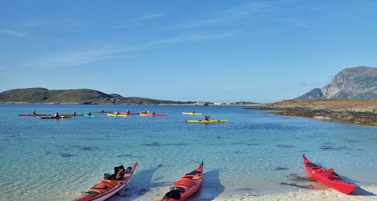 Les kayaks de mer reposent sur une plage de sable blanc tandis que les pagayeurs explorent une baie turquoise aux eaux cristallines.