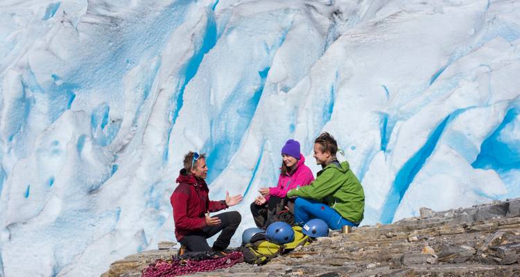 Le guide et les randonneurs font une pause sur des rochers à côté d'un mur de glacier bleu éclatant.