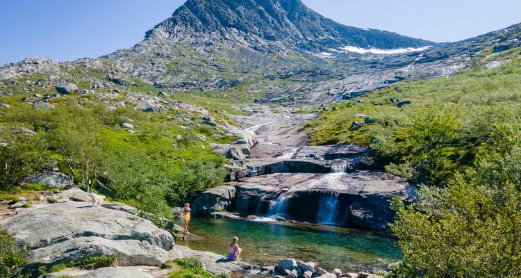 Les randonneurs apprécient un bassin alpin cristallin alimenté par une petite cascade sous une montagne escarpée.