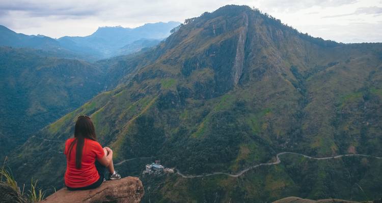 Una persona sentada en una roca con vista a una carretera de montaña.