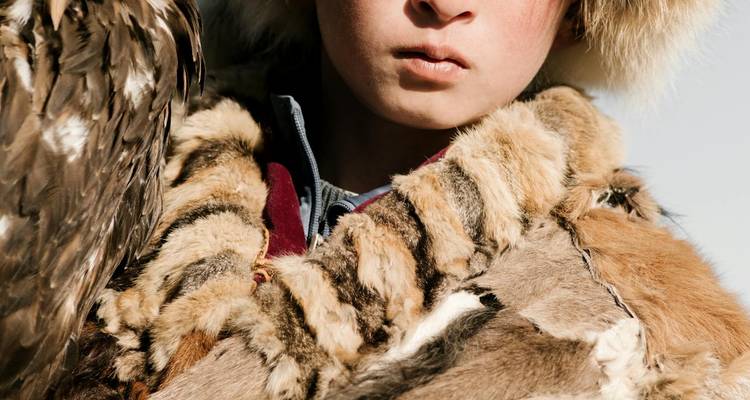 Primer plano de una persona vistiendo ropa de piel, sosteniendo un ave rapaz.