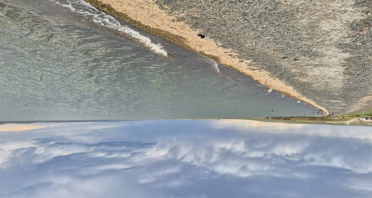 Una vista serena junto al lago con una orilla de guijarros bajo un cielo nublado.