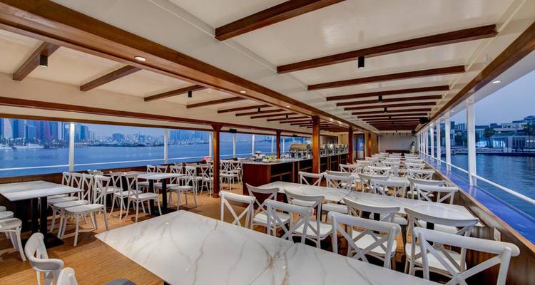 Comedor vacío en un barco con vista a la ciudad.