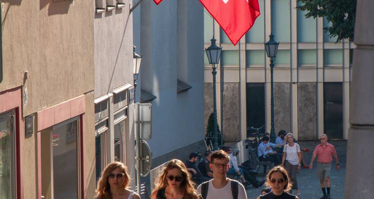 Des gens marchant près d'une rue avec un drapeau suisse au-dessus.