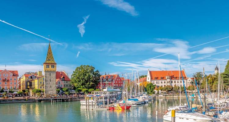 Farbenfrohe Hafengebäude und der spitz zulaufende Mangturm säumen den mit Segelbooten gefüllten Hafen an einem klaren Tag.