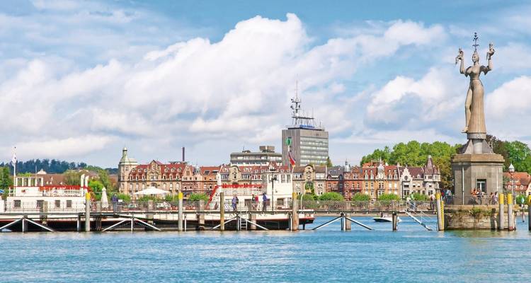 Hafenfront von Konstanz mit der rotierenden Imperia-Statue und historischen Gebäuden unter zerstreuten Wolken.