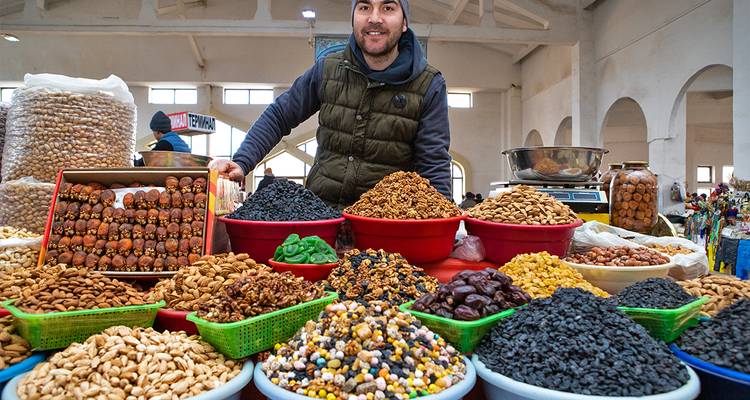 Puesto de mercado con una variedad de frutos secos y un vendedor sonriendo.