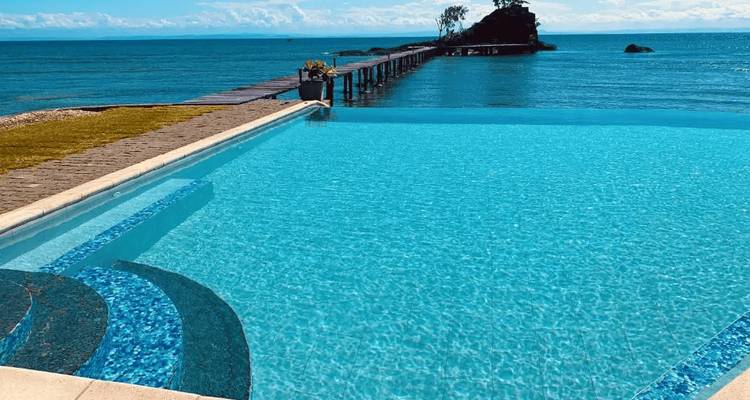 Piscina infinita con vista al océano con un muelle de madera que se extiende hacia el mar.