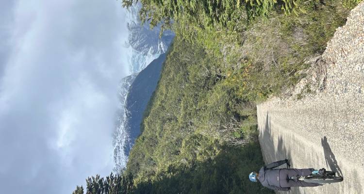 Cycliste sur un sentier forestier avec des montagnes enneigées en arrière-plan.