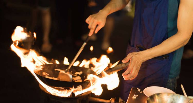 Street-food chef tosses ingredients in a flaming wok at night market.